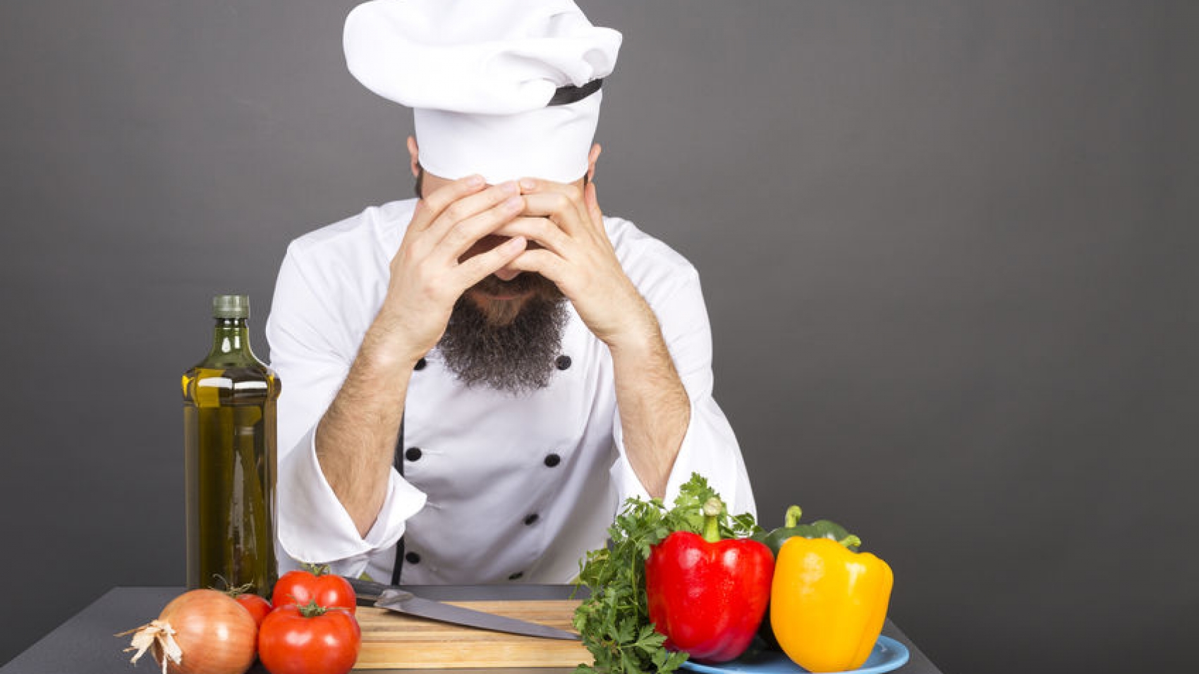 Young chef covers face with hands, having problems, isolated on gray